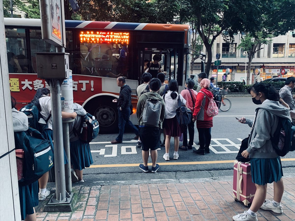 穿制服的學生在公車站牌前排隊等候上車