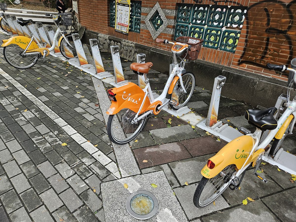 人行道旁的 YouBike 租借站，一整排橘白色自行車停在柱上